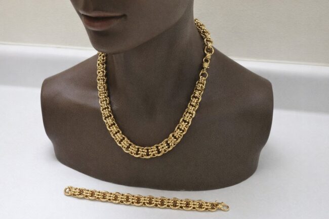Ett kraftigt bismarckhalsband i guld på en byst med matchande armband. Ett kraftigt bismarckhalsband i guld på en byst med matchande armband.